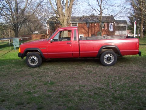 1991 Jeep Comanche - A red Jeep Comanche pickup truck is parked in a grassy yard with a house in the background.