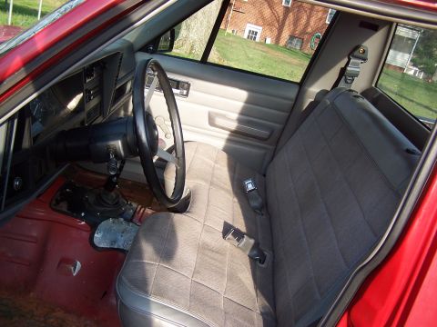 1991 Jeep Comanche - The interior of a red 1991 Jeep Comanche features a quilted fabric seat and a manual transmission shifter.