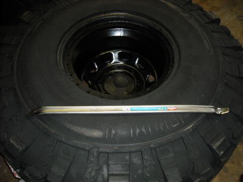 1979 Ford F-150 - Tire and rim assembly with a tire iron. The tire has some markings on its sidewall.