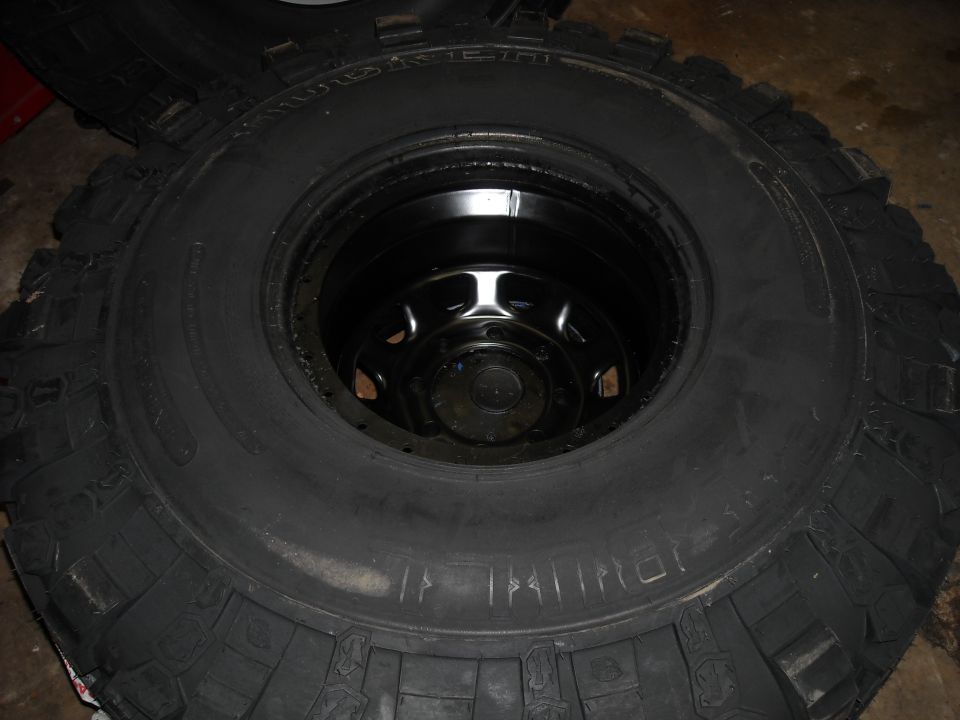 Close-up of a large off-road tire with a black rim inside. Some chalk marks are visible on the tire sidewall