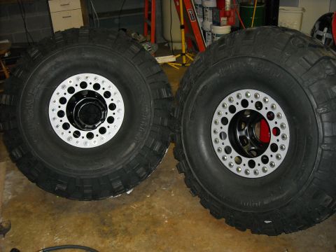 1979 Ford F-150 - Two large off-road tires with custom multi-hole silver and black wheels are shown side-by-side on a concrete floor.