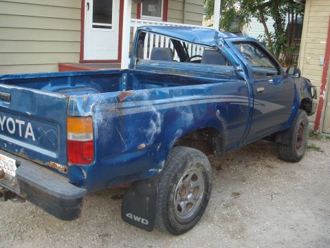 1991 Toyota Tacoma - This blue Toyota pickup truck, likely from the late 1980s, shows significant damage to its roof and body panels.