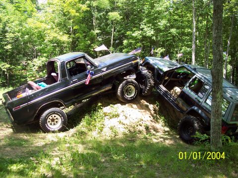 1979 Ford Bronco - Two off-road vehicles, a Ford truck and a Jeep, navigate a challenging dirt incline in a wooded area.