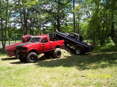 1979 Ford Bronco - Two lifted trucks and a red car are parked on a grassy hill with trees in the background. A date stamp shows 01/01/2004.