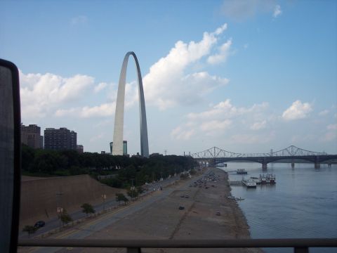 1960 Ford Falcon - The Gateway Arch stands tall against a partly cloudy sky, with the Mississippi River flowing beside it.