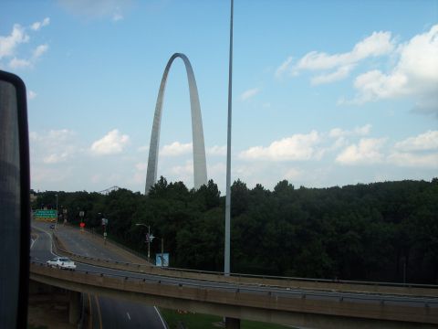 1960 Ford Falcon - A white sedan drives on a highway with the Gateway Arch visible in the distance under a cloudy sky.