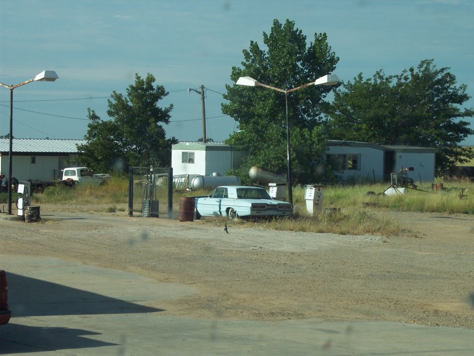 Light blue 1960s sedan parked at a gas station, rear view