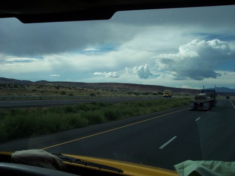 1960 Ford Falcon - A view from a vehicle driving on a highway, with trucks visible in the distance under a dramatic sky.