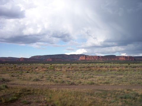 1960 Ford Falcon - A vast desert landscape unfolds with dramatic mesas under a dramatic sky, hinting at a journey through arid terrain.