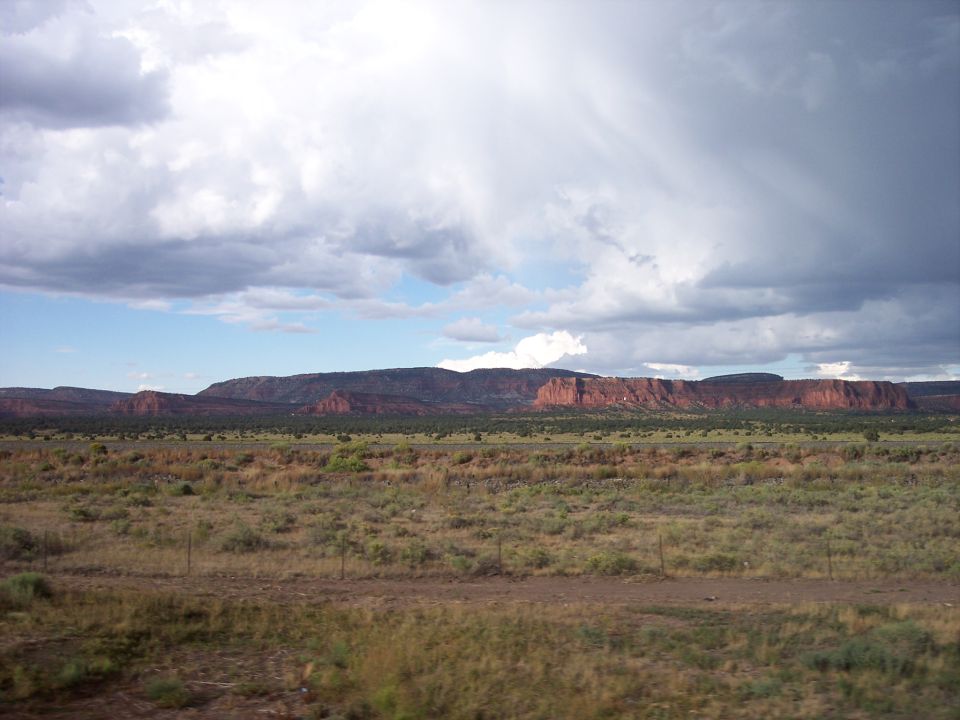 Wide shot of desert mesas under a cloudy sky, with dry grass and brush in the foreground