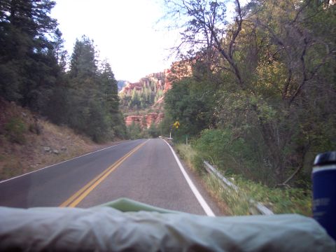 1960 Ford Falcon - Driving through a scenic canyon with trees lining the road and red rock cliffs in the distance.