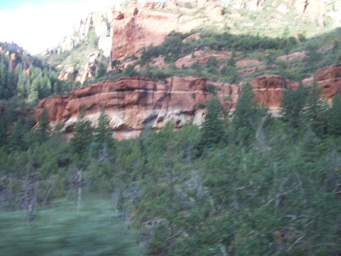 1960 Ford Falcon - A scenic view of layered red rock cliffs and green trees, with a blurred foreground suggesting motion.