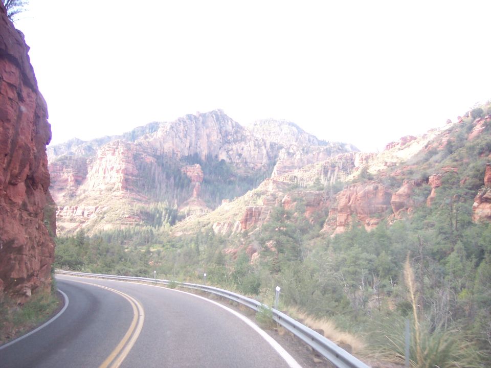 Curving road passes red rock cliffs and mountains under a bright sky