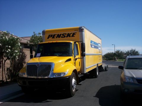 1960 Ford Falcon - A Penske box truck is parked on a paved surface next to a silver SUV under a clear blue sky.