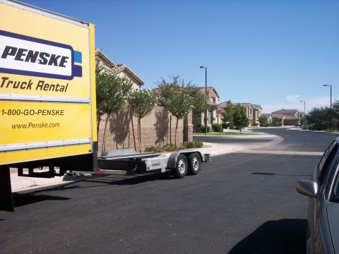 1960 Ford Falcon - A Penske truck is parked next to a car trailer on a sunny day in a residential area.