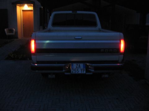 1990 Ford F-150 - Rear view of a white 1990 Ford F-150 pickup truck with its taillights on, parked on a brick driveway.