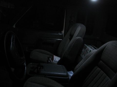1990 Ford F-150 - The dimly lit interior of a vehicle shows fabric seats, a steering wheel, and a center console, with a box visible on the passenger seat.