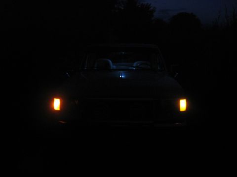 1990 Ford F-150 - A dark 1987 Ford F-150 pickup truck is seen from the front at night, its headlights illuminating the darkness.