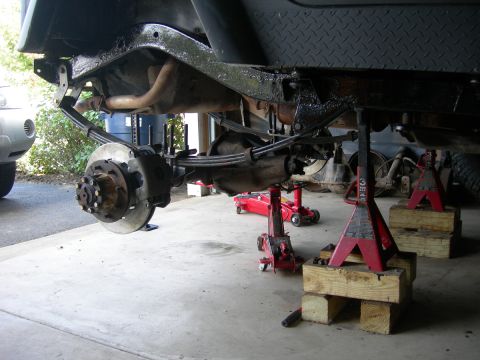 1991 Jeep Wrangler - The underside of a Jeep Wrangler is elevated on jack stands for maintenance, revealing its suspension and axle components.