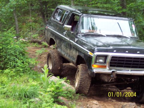 1979 Ford Bronco - This Ford Bronco is navigating a rough, wooded trail with significant ground clearance.