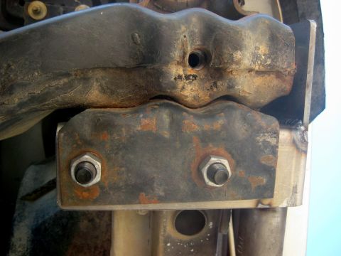 1996 Ford Bronco - This is a close-up view of a heavily rusted metal bracket with visible bolts and some welding.