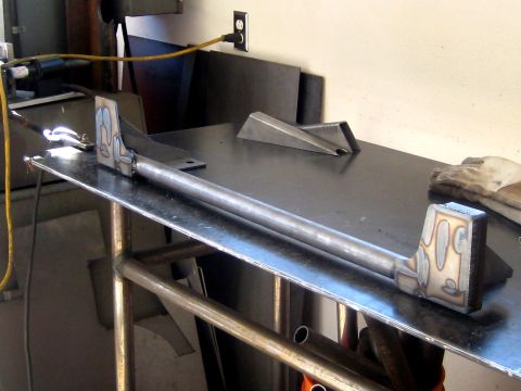 1996 Ford Bronco - A fabricated metal bar with welded brackets sits on a workbench, possibly a custom automotive part.