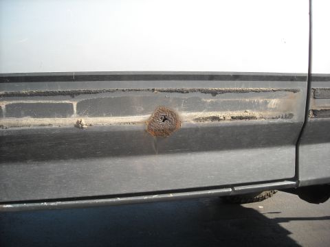 1990 Ford C-150 (Centurion Conversions) - A close-up view of rust damage on the side panel of a vehicle.