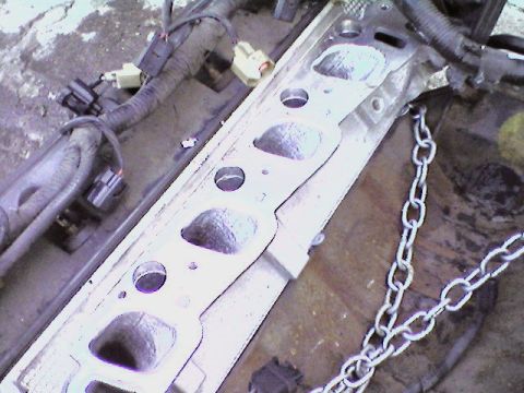 1998 Ford Crown Victoria - Close-up of an engine's intake manifold gasket and associated wiring, with a metal chain in the foreground.