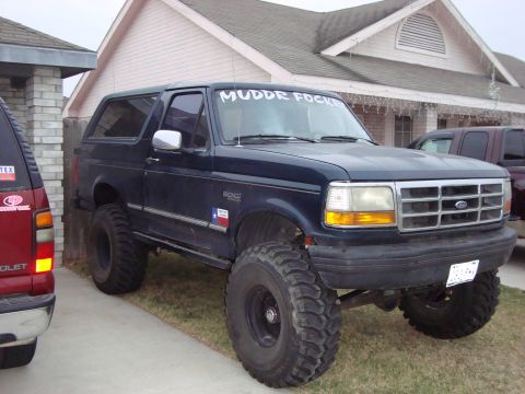 1995 Ford Bronco - This lifted Ford Bronco is parked in a driveway next to another SUV, ready for off-road adventures.