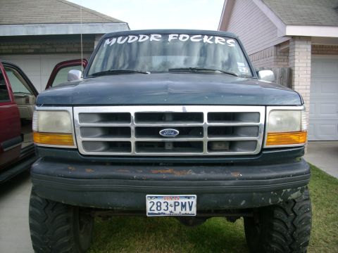 1995 Ford Bronco - This lifted Ford Bronco has a custom windshield banner and is parked in front of a garage.