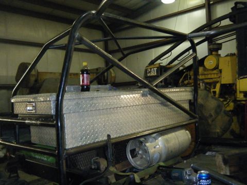 1978 Ford Bronco - A custom roll cage is installed over toolboxes and a propane tank, with heavy machinery visible in the background.