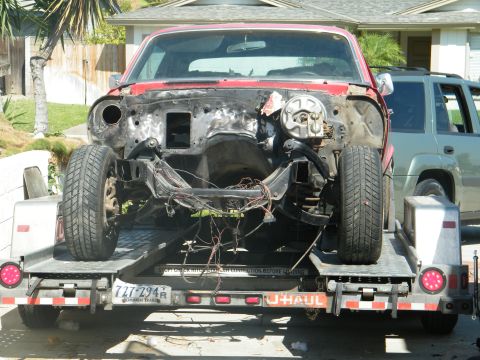 1982 Ford Bronco - A red vehicle chassis is transported on a U-Haul trailer, revealing its internal structure and missing components.