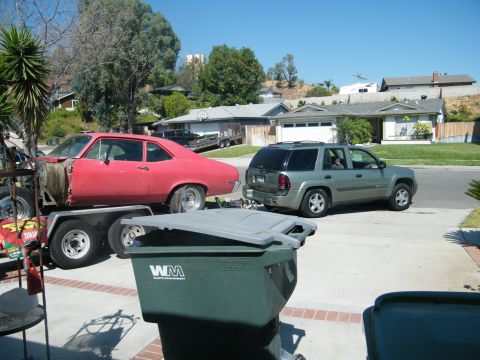 1982 Ford Bronco - A red car is being towed on a trailer by a green SUV on a sunny day.
