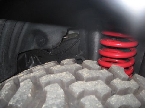 1990 Ford Bronco - Detail of a red coil spring and aggressive tire tread within a vehicle's wheel well.