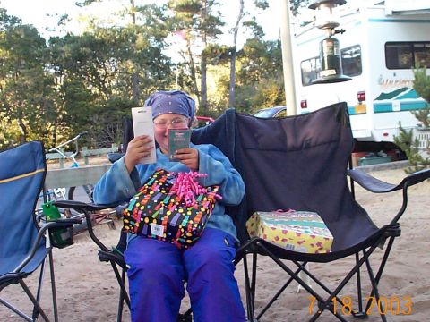 1987 Ford Supercrewzer - A person sits in a camping chair surrounded by gifts, with an RV visible in the background at a campsite.