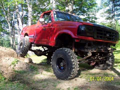 1979 Ford Bronco - This modified pickup truck is shown off-roading on a dirt hill with trees in the background.