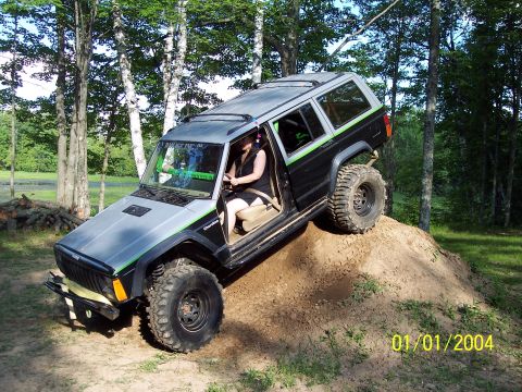 1979 Ford Bronco - A Jeep Cherokee XJ navigates an off-road obstacle with its driver visible.