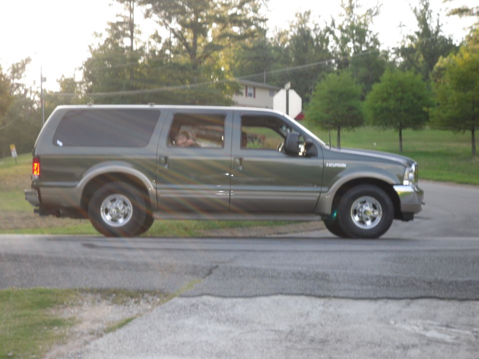 Side view of a dark green and tan Ford Excursion SUV driving on a road