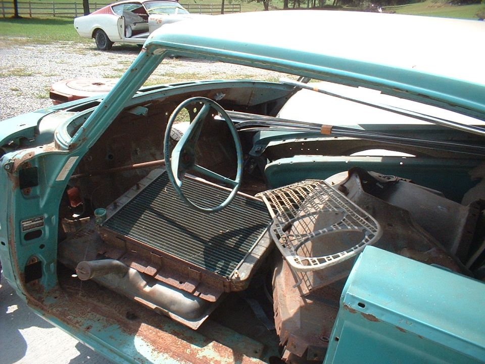 Teal disassembled classic Ford project car interior with rust, steering wheel, and stacked parts