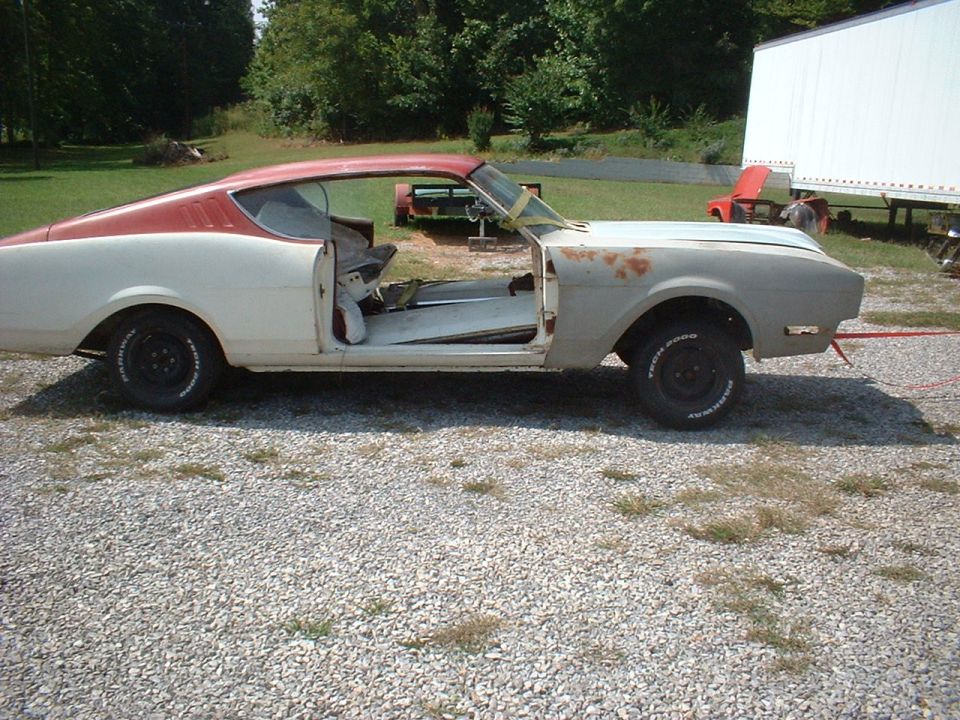 White fastback coupe project with red roof, door open, gutted interior, on gravel