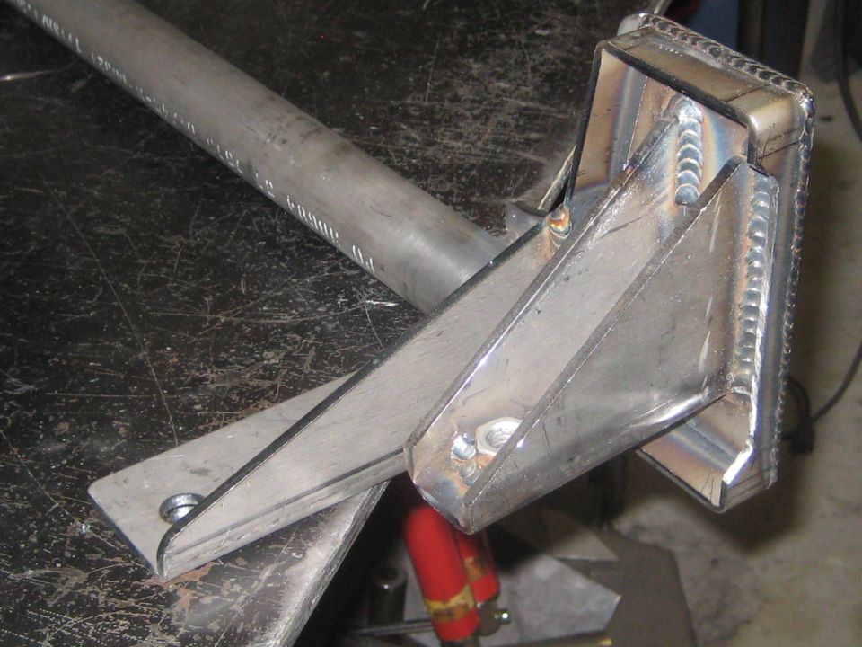 Welded metal bracket with a tubular extension, resting on a dark, scratched surface