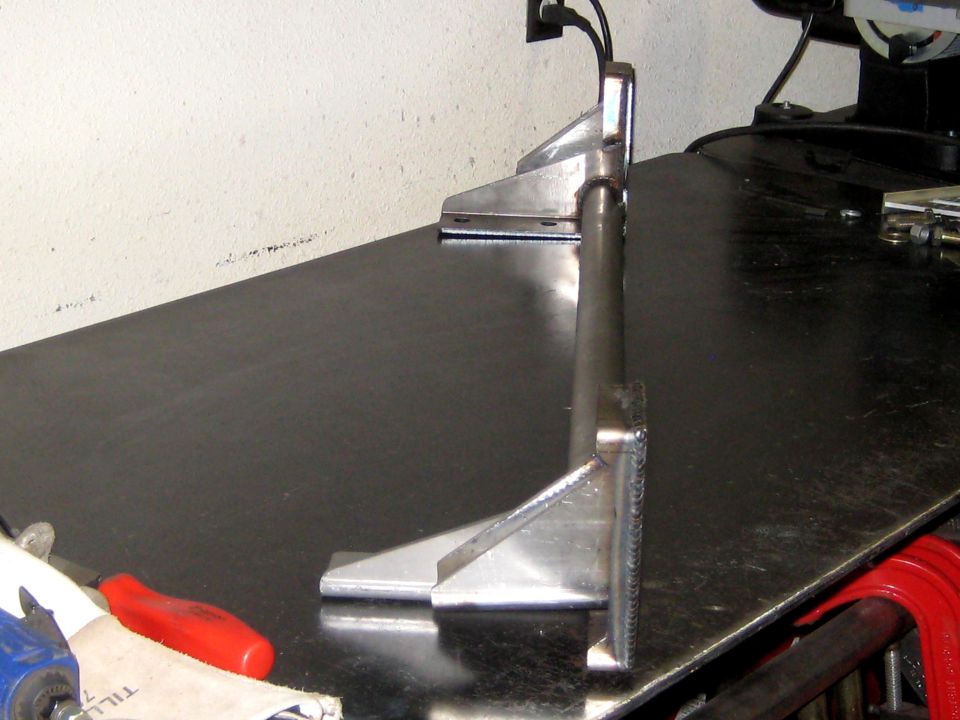 Metal bracket with welded joints on a dark workbench surface, with tools nearby