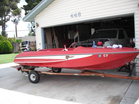 1991 Ford Bronco - A red boat with a white stripe is parked on a trailer in front of an open garage containing a truck.