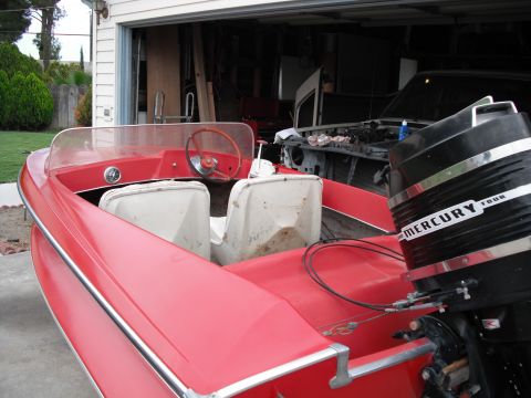 1991 Ford Bronco - A red boat with a Mercury outboard motor is parked in front of an open garage, where another vehicle is visible.