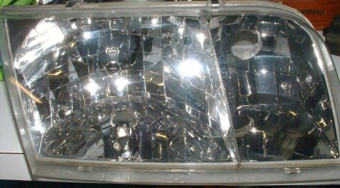 2004 Ford Crown Victoria - A complete clear-lens headlight assembly sitting face-up on a table indoors, showing the multi-faceted chrome reflector, low and high beam…