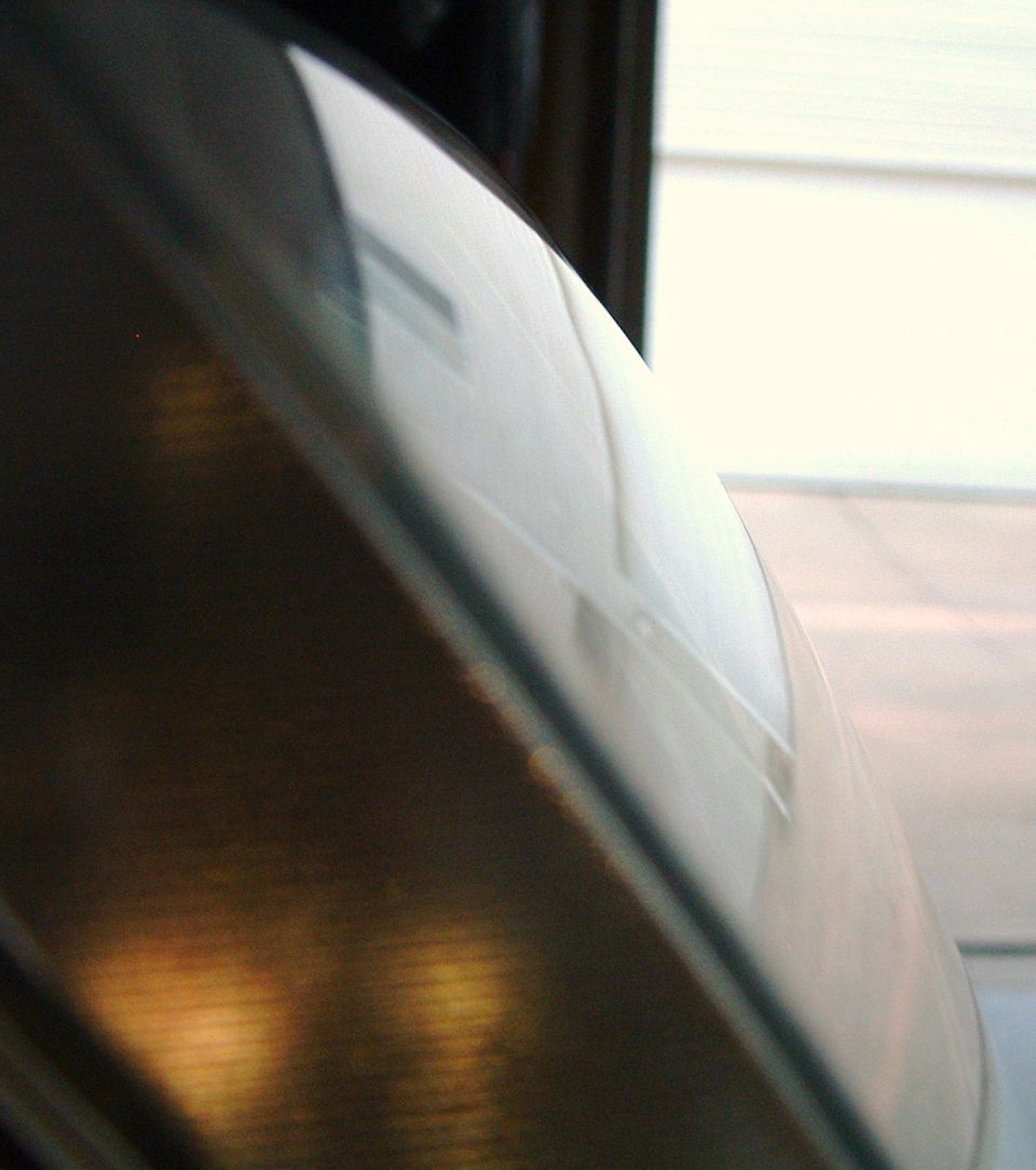 Edge-on close-up of a polished headlight lens with amber reflections and fine sanding marks