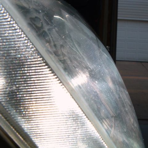 2004 Ford Crown Victoria - Sunlit macro of a headlight lens edge showing the fine vertical fluting of the side-marker section next to a hazed, scratched outer cover s…