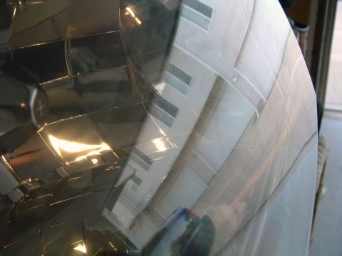 2004 Ford Crown Victoria - Angled close-up of a clear headlight lens held up in a garage doorway, with the chrome faceted reflector glowing gold on the left and the p…