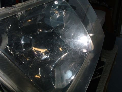 2004 Ford Crown Victoria - Extreme close-up of a clear plastic headlight lens removed from the car and held indoors, with faceted reflector segments and a blacked-out…