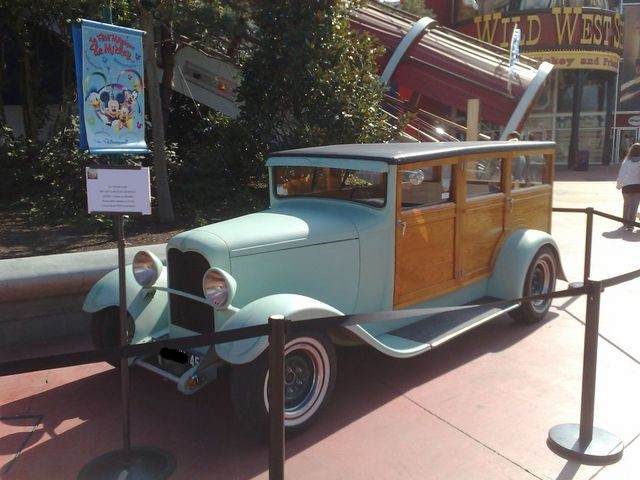 Light blue and wood-paneled station wagon parked outdoors, with a banner and sign in front